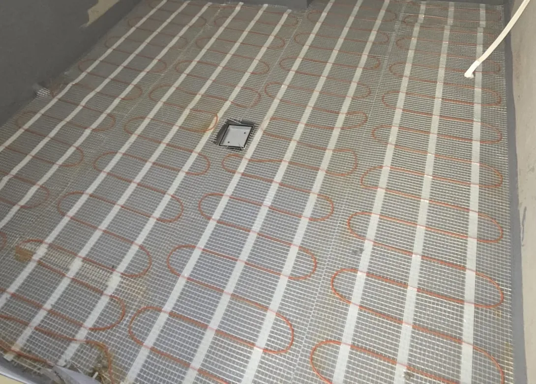 Mesh backed heating cable covering an ensuite floor, trimmed neatly around the chrome waste grate.