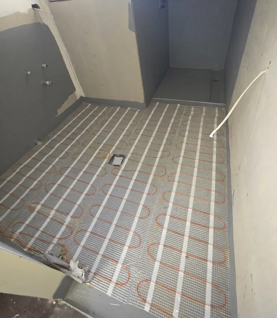 A heating mat laid over the finished waterproofing of a bathroom floor, with the floor waste left clear.