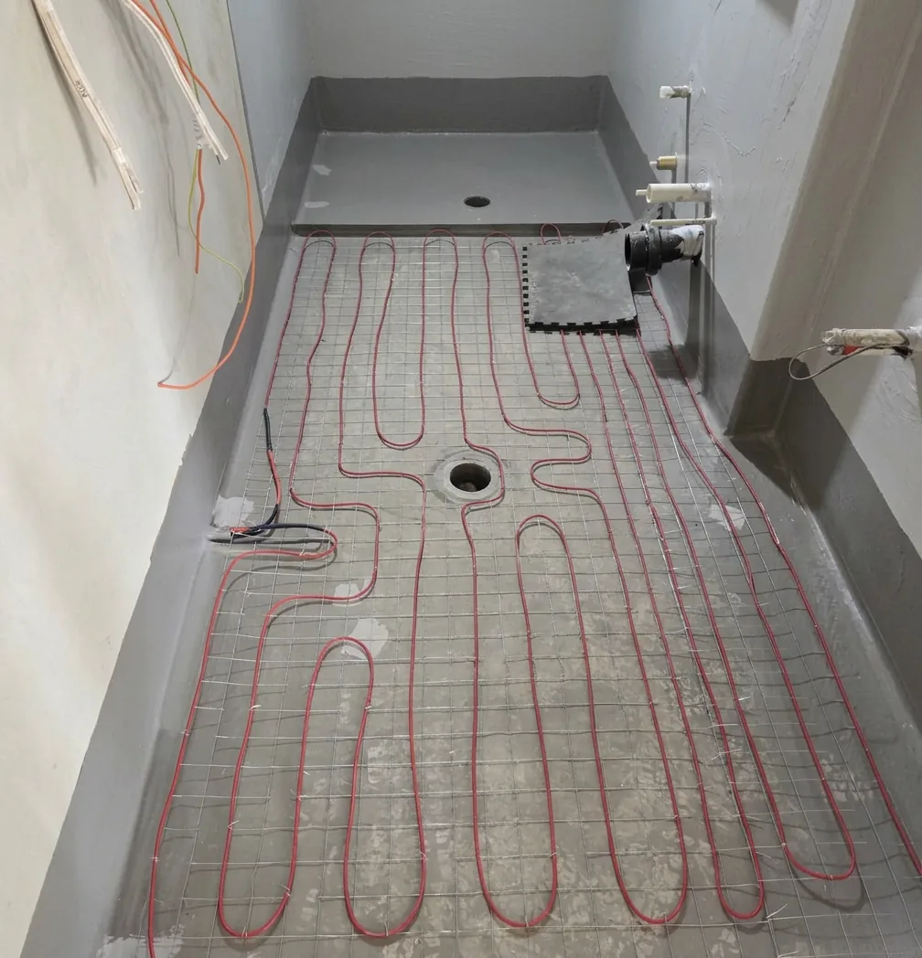 Cable laid across a long narrow bathroom floor, with the shower base in and conduits run up the wall.