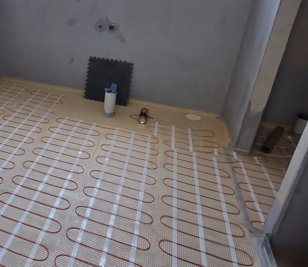 A heating mat covering the floor of an amenity room, with a float and a tube of adhesive standing against the wall.